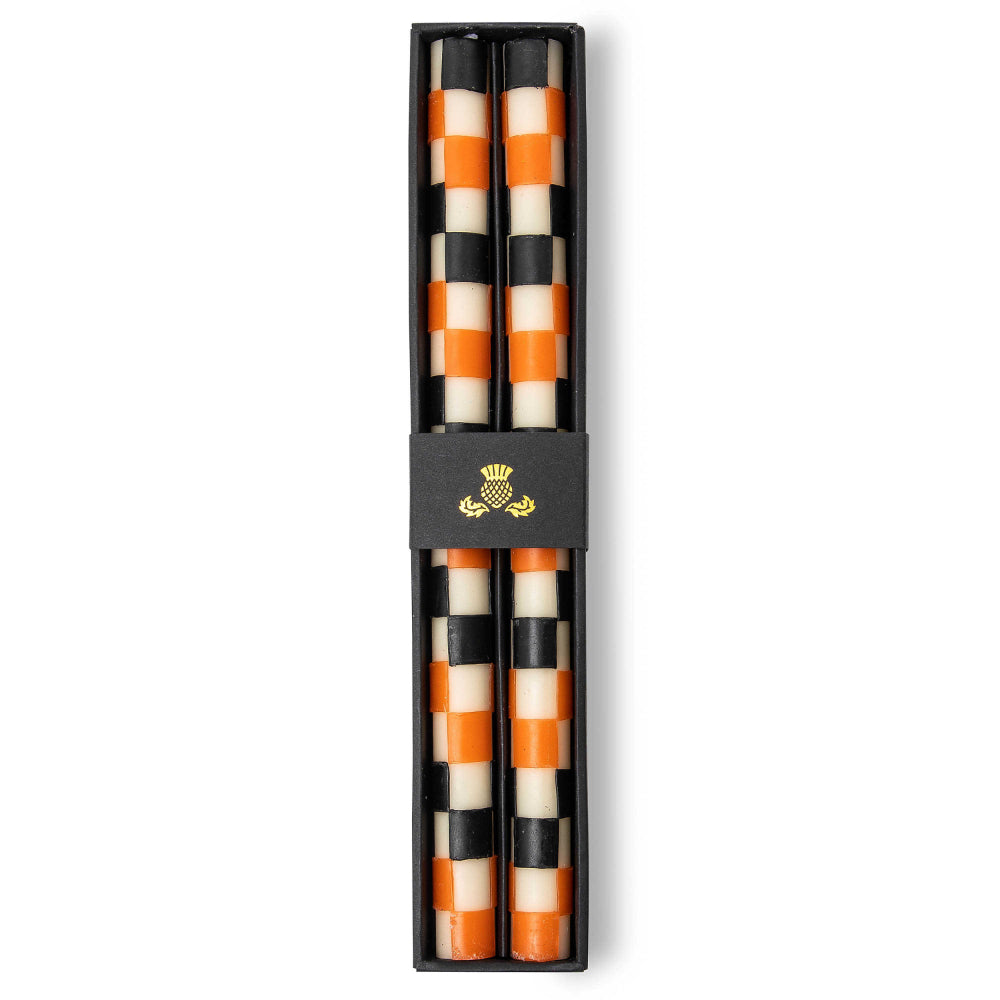 Pair of boxed checkered candles with black, orange, and beige pattern in glass holders on a white background