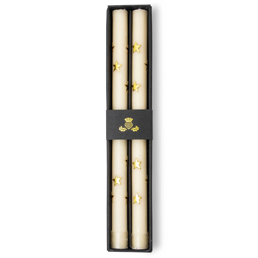 Two boxed beige candles with gold star patterns in a black box with a clear top on a white background
