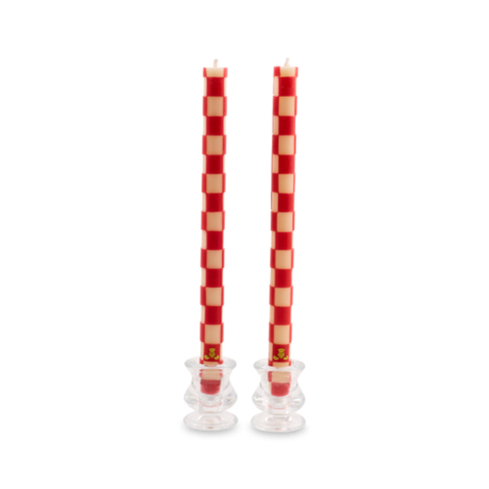 Two tall red and cream checkered taper candles standing in clear glass candle holders against a white background.