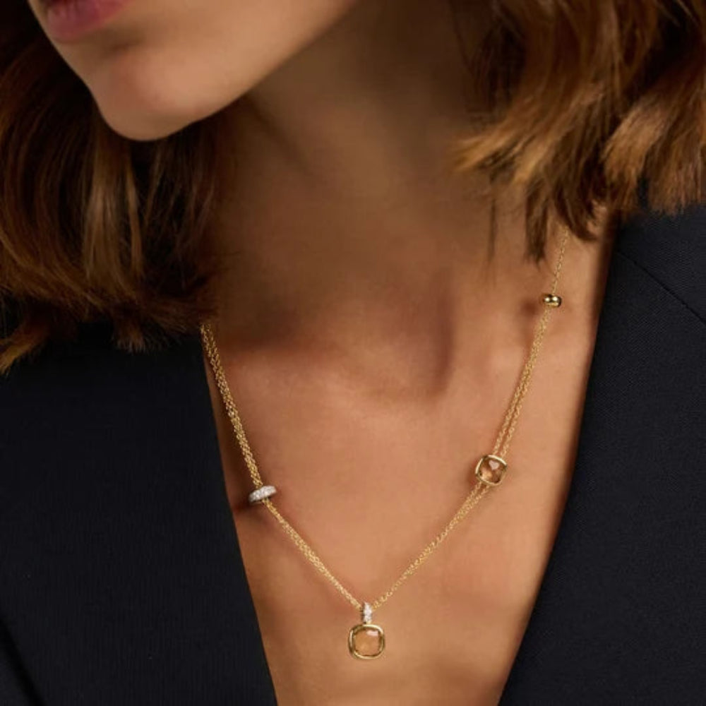 A close-up of a model wearing a delicate gold layered necklace with a cushion yellow stones