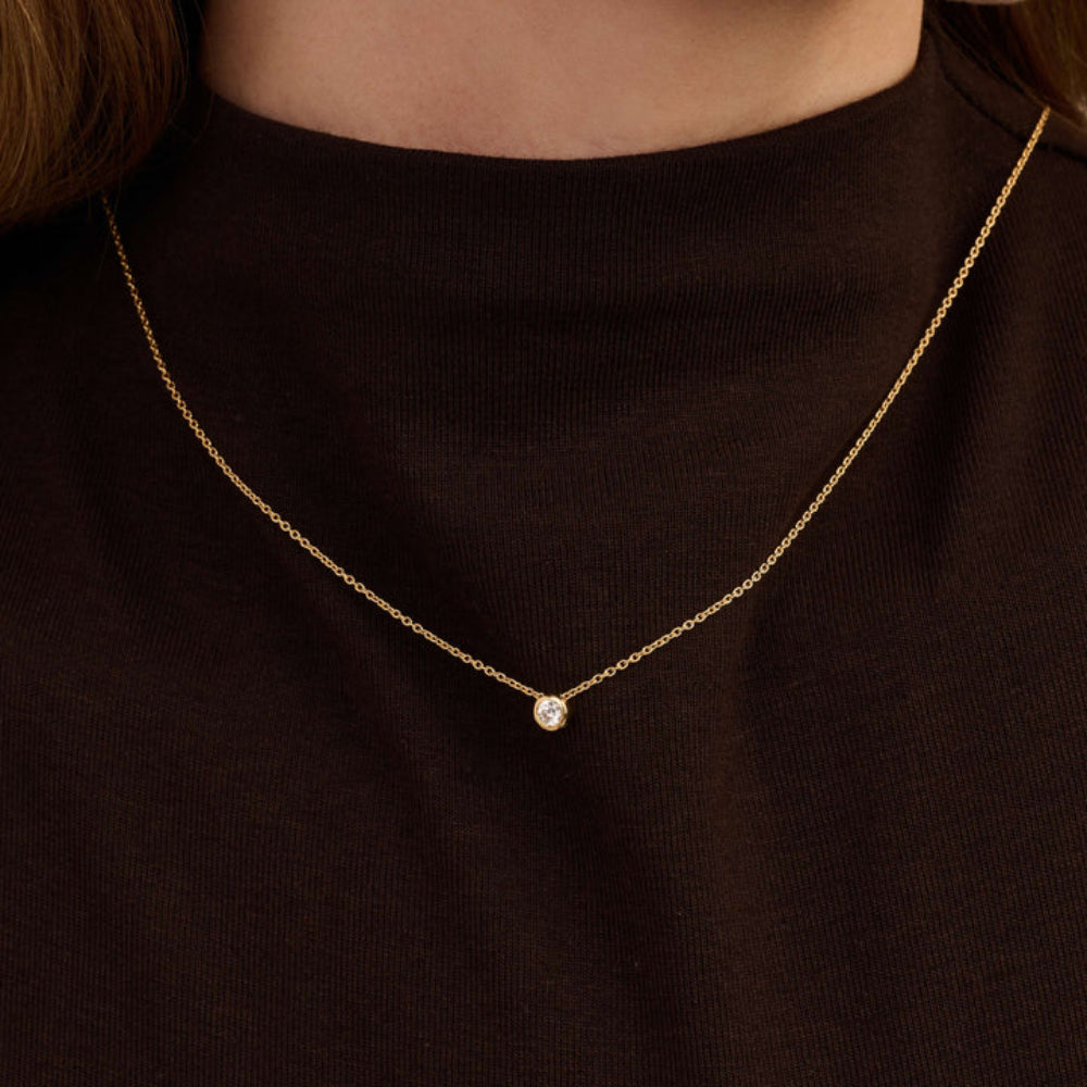 Gold necklace with a small pendant on a black background
