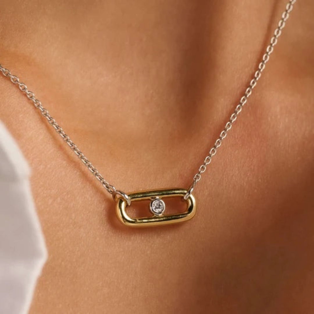 A close-up of a delicate necklace worn on a person's neck, featuring a gold oval pendant with a small clear gemstone and a silver chain.
