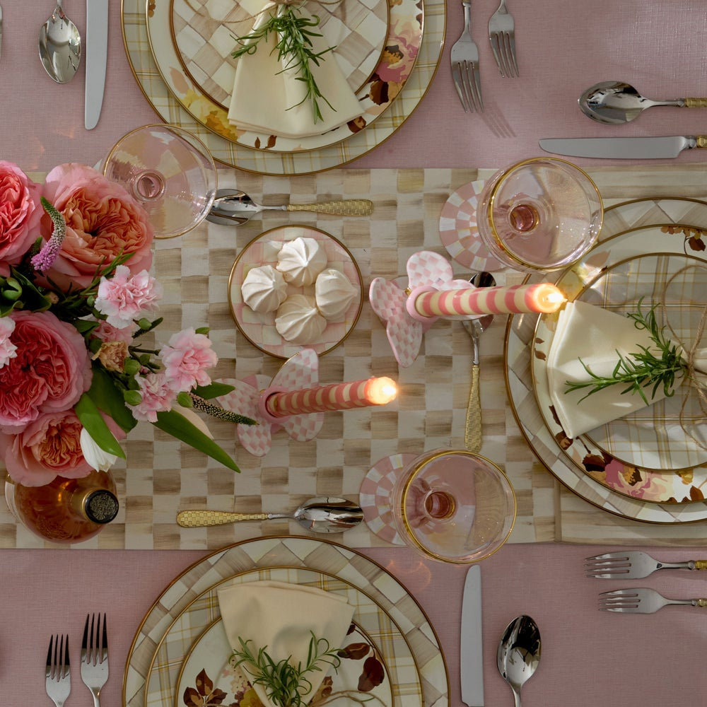 Elegant table setting with floral arrangements, candles, and decorative plates on a checkered tablecloth.