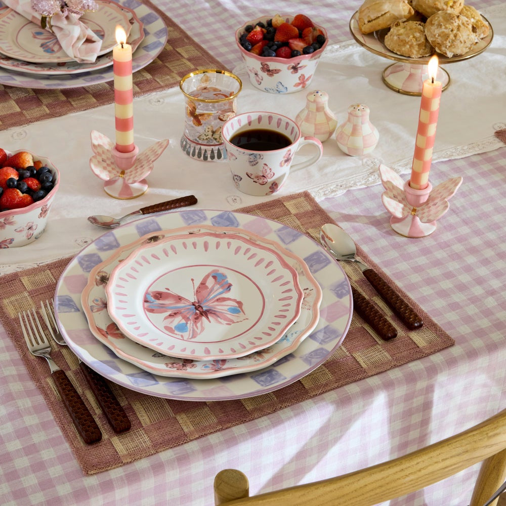 Café setting with butterfly-patterned plates, fruit bowls, and a cup of coffee on a checkered tablecloth.