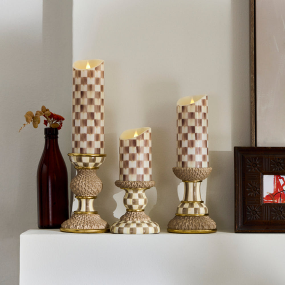 Decorative candles with checkered pattern on a shelf with a vase and photo frame.
