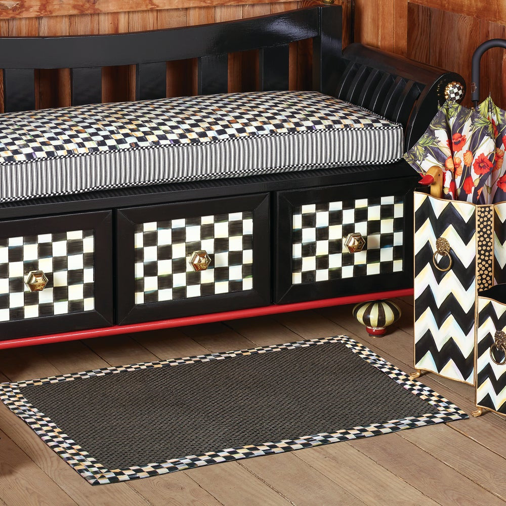 A black and white checkered bench with striped cushions, matching patterned drawer pulls, a black and white checkered rug, and a decorative umbrella stand holding a floral umbrella, set against a wood-paneled wall and floor.