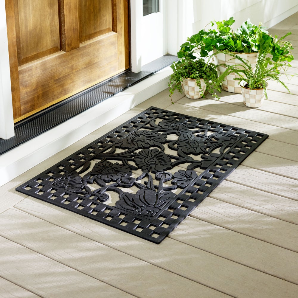 Decorative black doormat with floral patterns on a wooden floor in front of a wooden door.