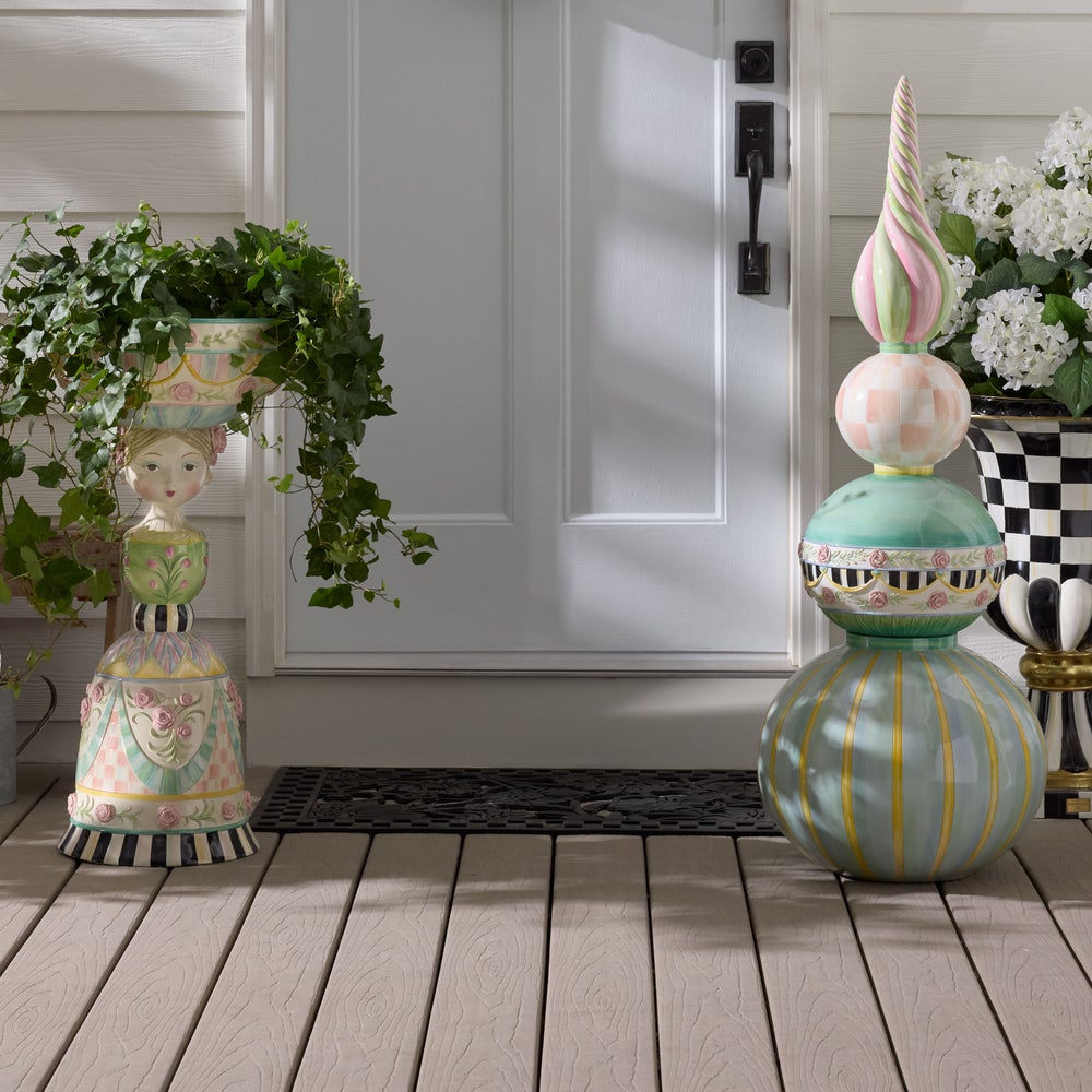 Decorative black doormat with floral patterns on a wooden floor in front of a wooden door with other outside decor.
