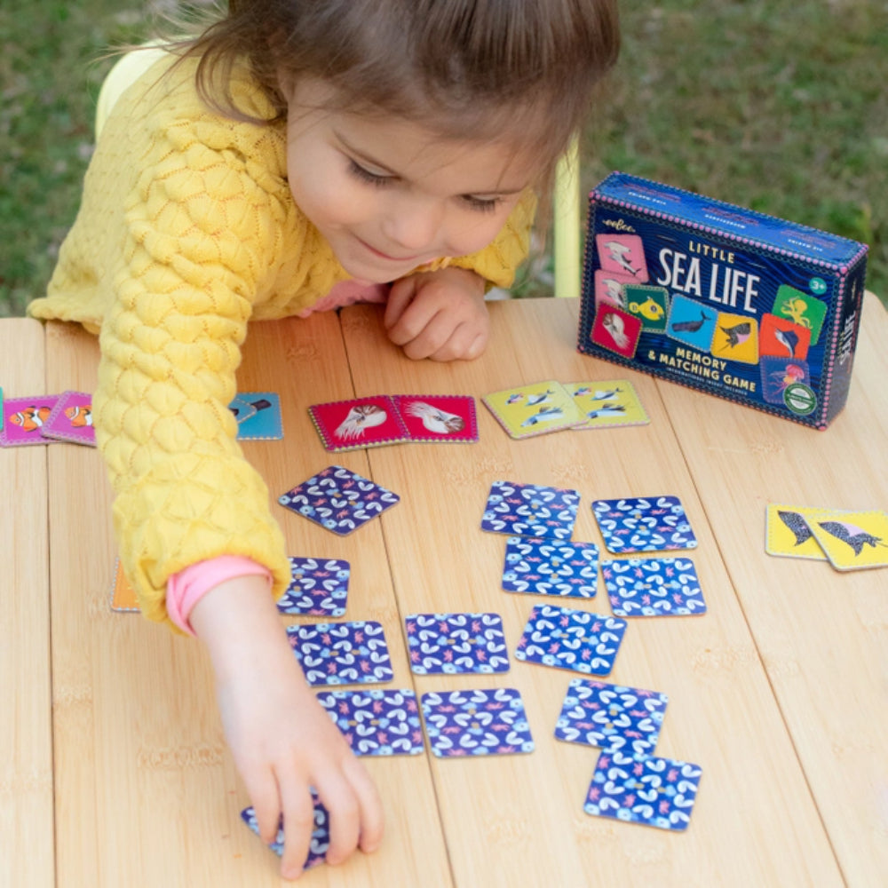 Child playing with a 'Little Sea Life' memory game on a wooden table.