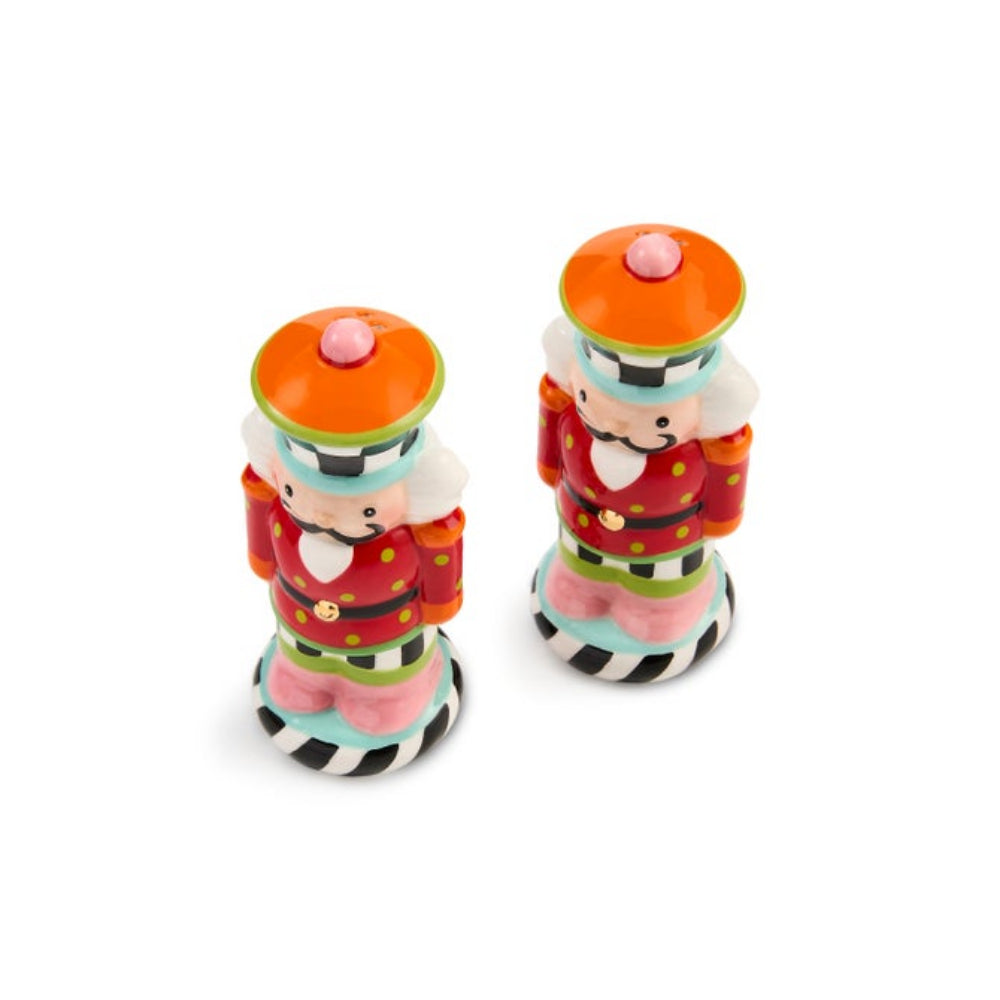 Two small nutcracker figurines standing side by side on a plain white background. Each nutcracker has an orange hat with a pink pom-pom, a red coat with gold polka dots, white beard, and black-and-white striped base.