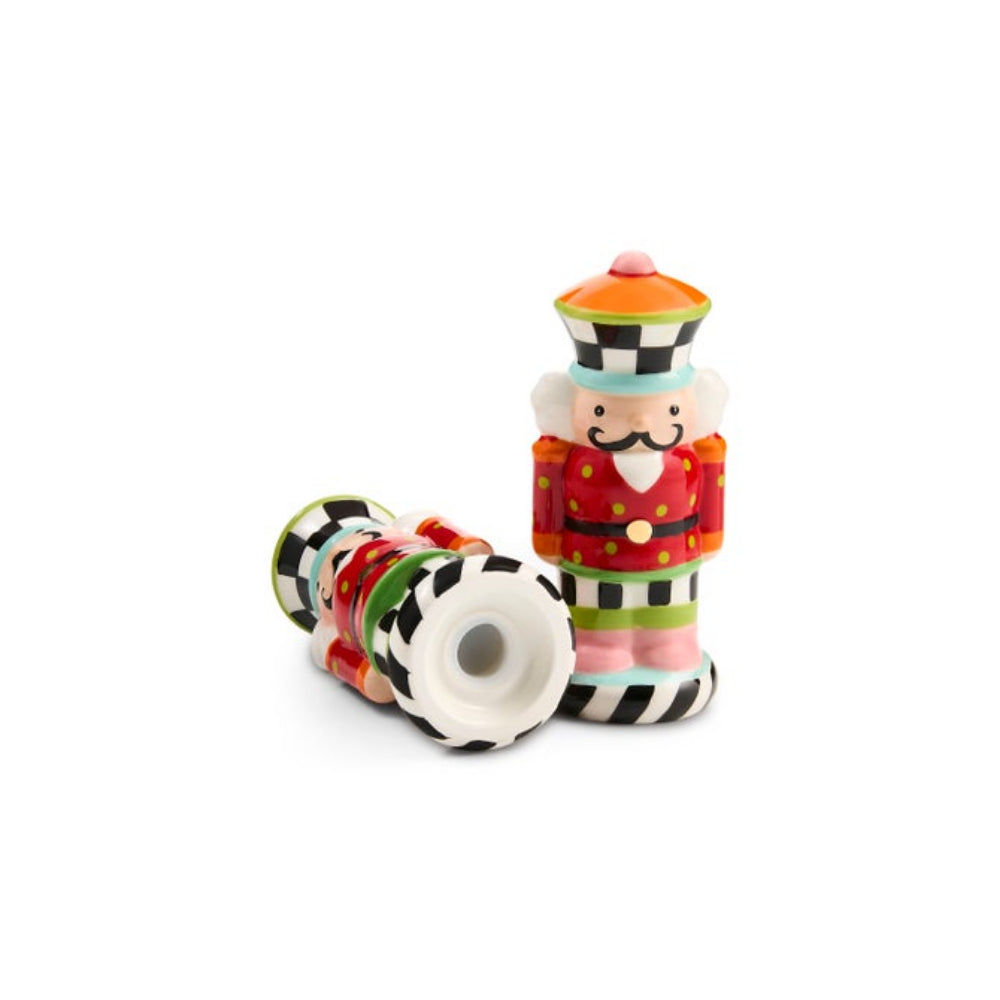 A pair of colorful ceramic nutcracker salt and pepper shakers on a plain white background. One shaker is standing upright in a red uniform with black-and-white striped accents, and the other lies on its side showing a white cylindrical chamber and striped base.