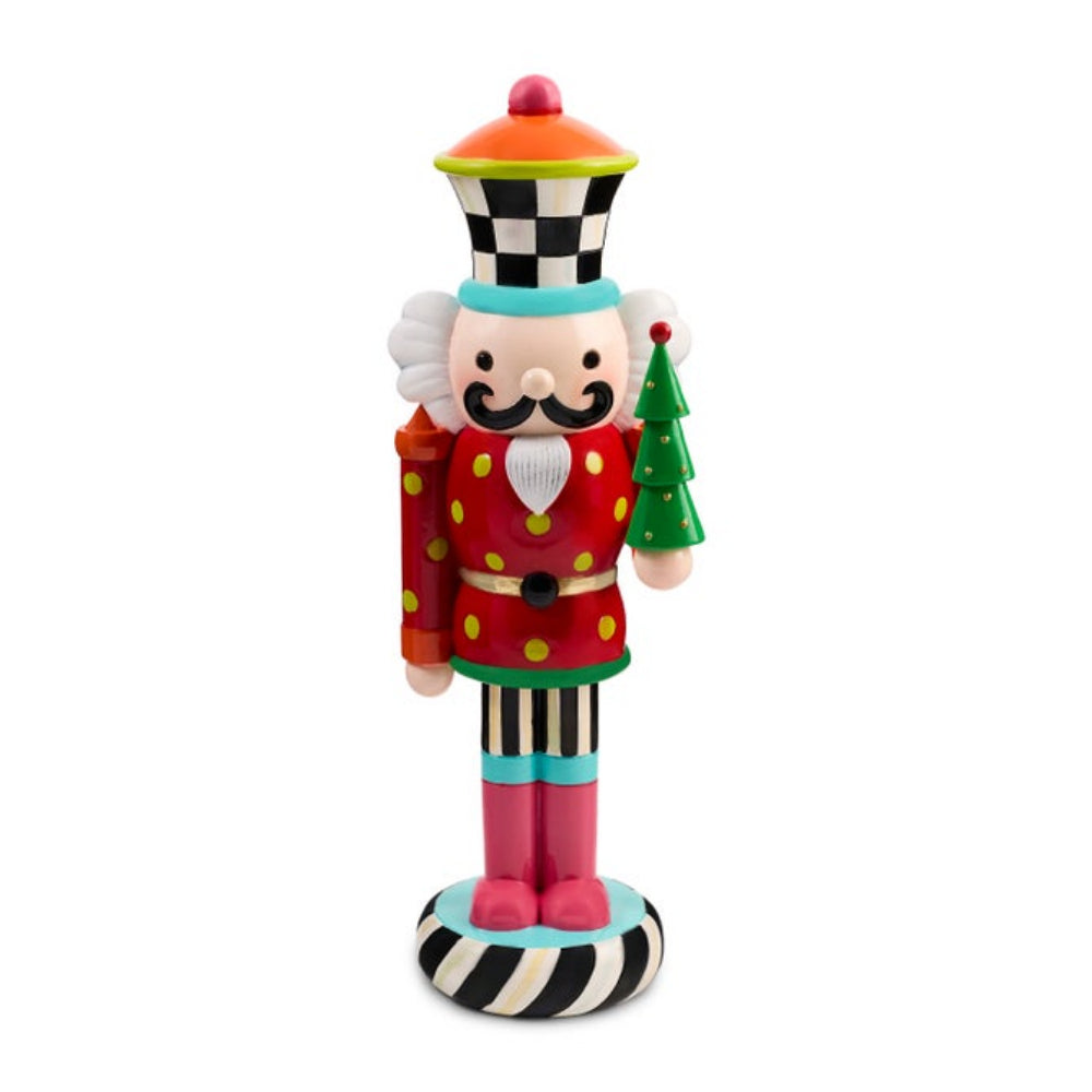 A colorful nutcracker figurine with a red polka-dot coat, striped legs, a checkered hat, and a small green tree, shown on a plain white background.