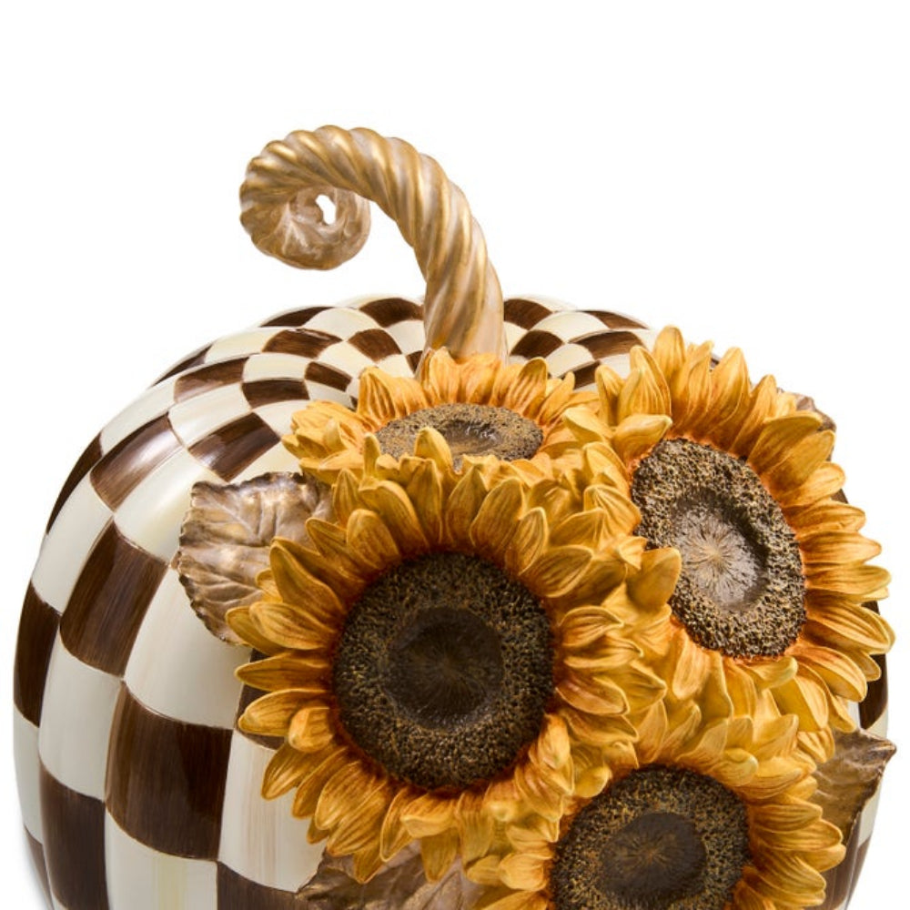 A decorative pumpkin sculpture with a brown and cream checkerboard pattern and three large yellow sunflowers in front, shown on a plain white background.