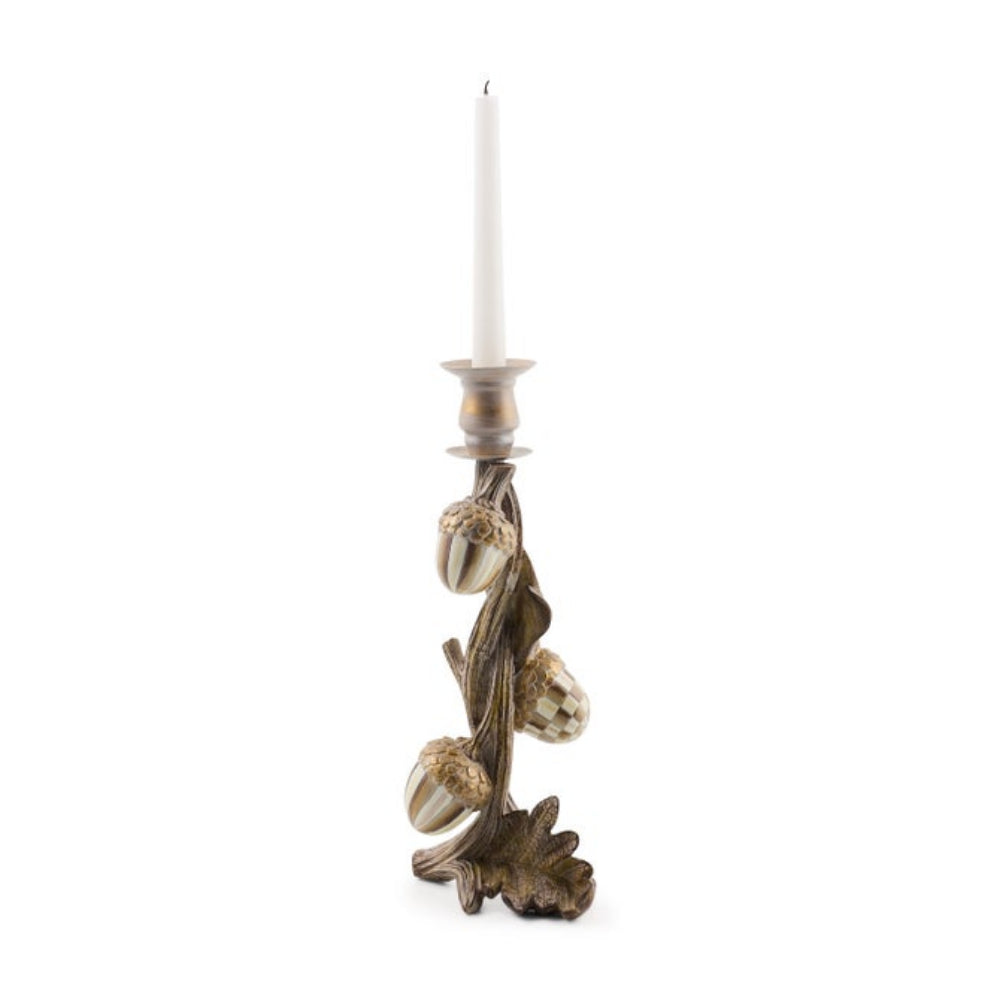 A decorative acorn-shaped candlestick holder with a twisted branch base, featuring three detailed acorns and a white taper candle inserted, set against a plain white background.
