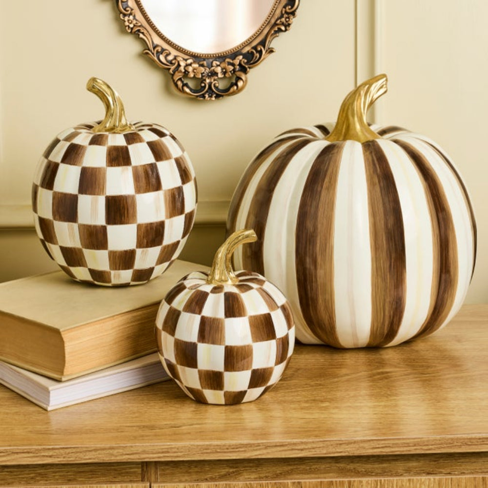 A group of Chocolate Check Pumpkins on a counter wooden display with books and a mirror in the background. 