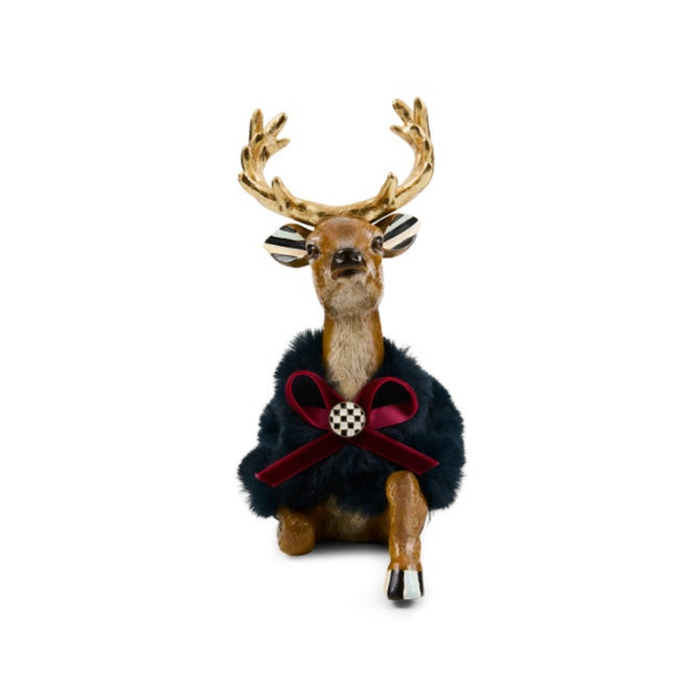 A decorative reindeer figurine with antlers, dressed in a dark navy blue faux-fur coat and a burgundy velvet bow with a checkered center, set against a plain white background.