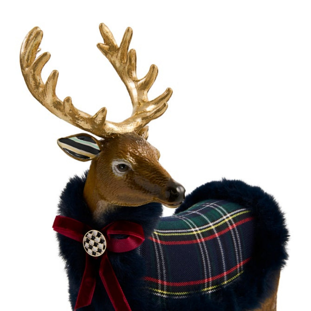A decorative deer figurine with large gold antlers, a brown head, a navy plaid draped wrap with red trim, a dark blue faux-fur collar, and a red bow with a checkered button accent, shown on a plain white background.