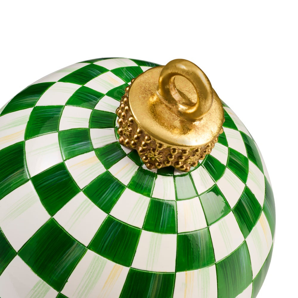 A close-up of a decorative spherical ornament featuring a green and white checkered pattern with a textured gold finial on top, set against a plain white background.