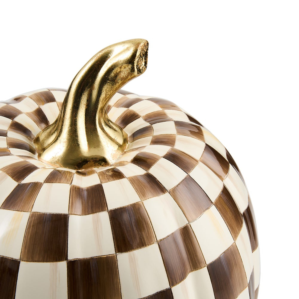 A close-up of a decorative pumpkin with a brown and cream checkered pattern and a metallic gold stem, shown against a plain white background.
