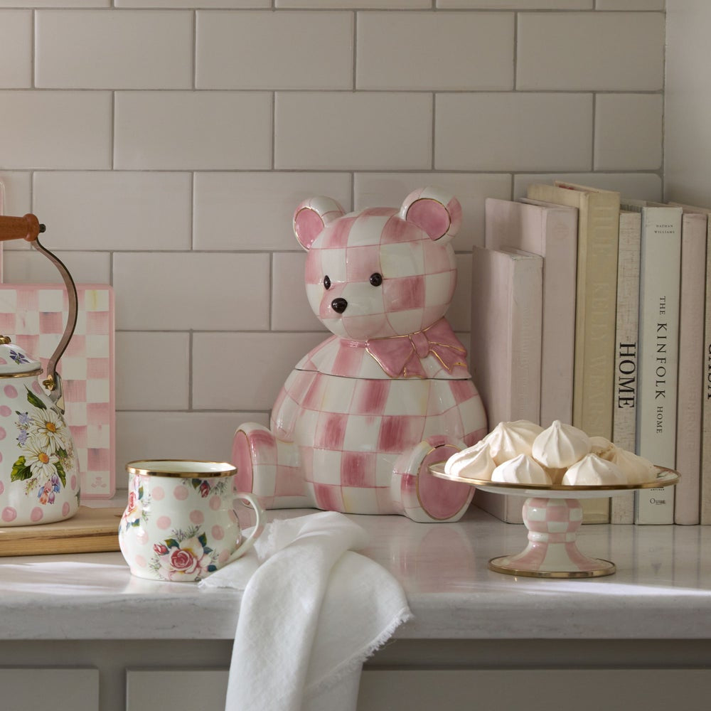 Checkered bear teapot on a kitchen counter with books and a teacup in the background.