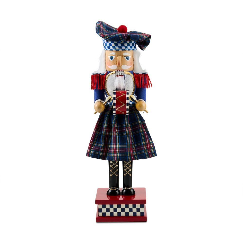 A traditional Scottish kilted nutcracker figurine standing on a red base with a checkered front panel, wearing a tartan kilt, matching hat, and red-and-white striped jacket against a plain white background.