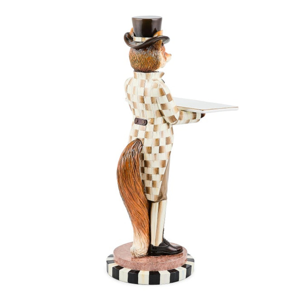 A decorative figurine of a fox dressed as a waiter, standing on a striped black-and-white base and holding a tray. The fox has a brown tail and face, with a cream and brown checkered outfit and a black top hat, photographed on a plain white background.