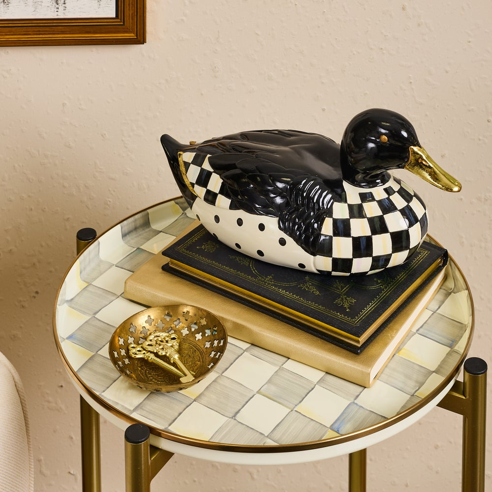 A decorative duck figurine with a black-and-white checkerboard pattern and a gold beak, displayed on stacked books on a small round table.