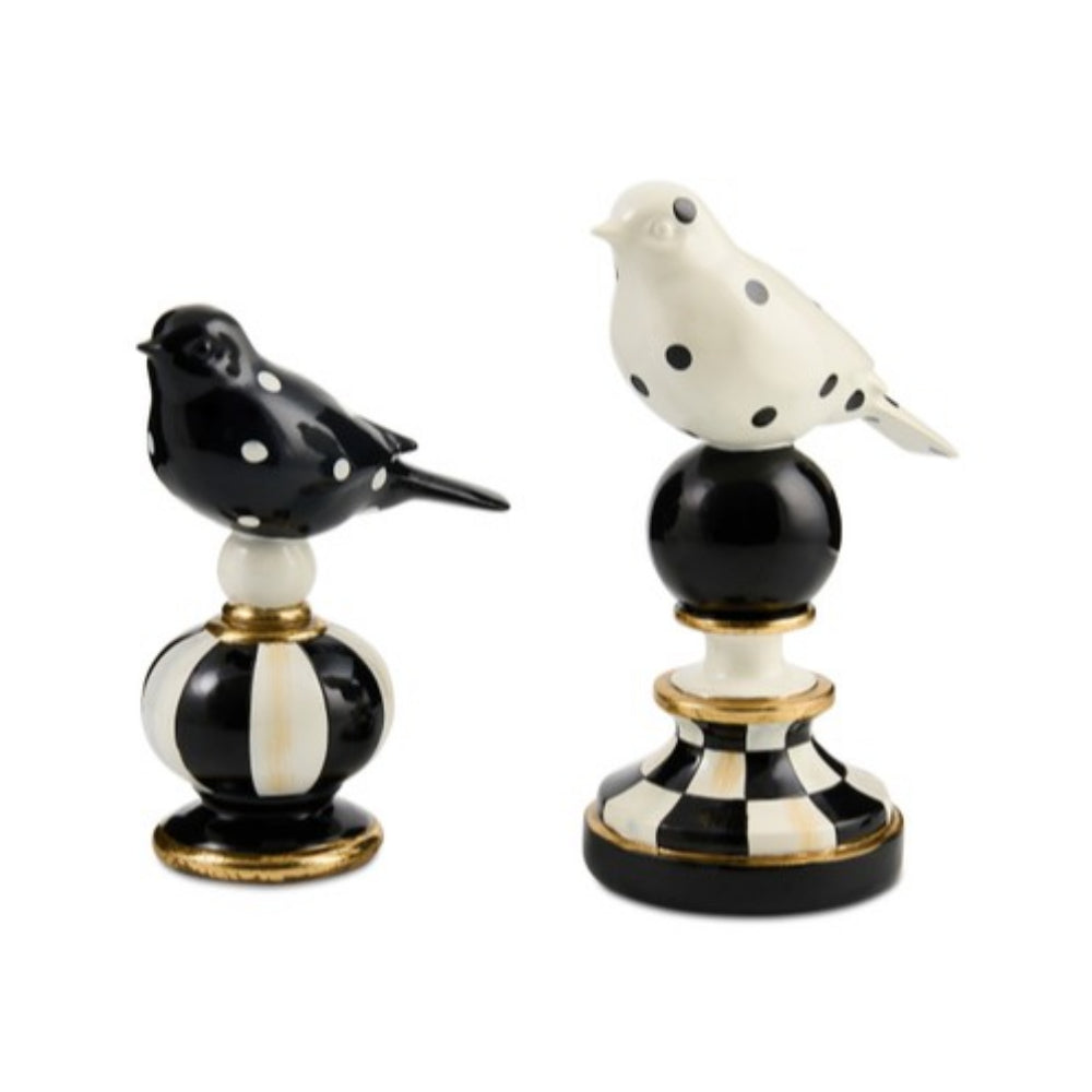 Two decorative bird figurines on a white background. One bird is black with white polka dots and sits on a white and black striped pedestal with gold trim.
