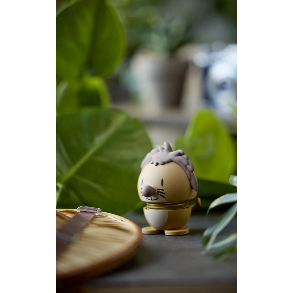 Tan lion shaped figurine with a spring on a table with green plants and other objects made to look like a safari on a brown table 