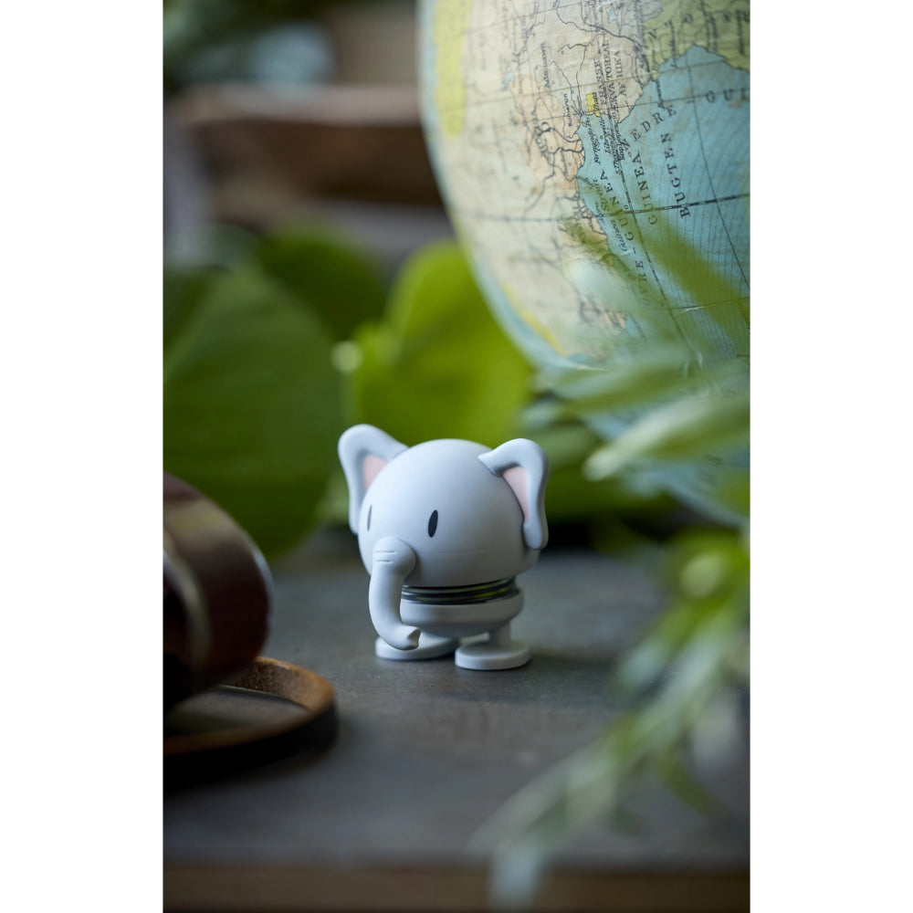 Small elephant figurine on a table with a globe and leaves in the background