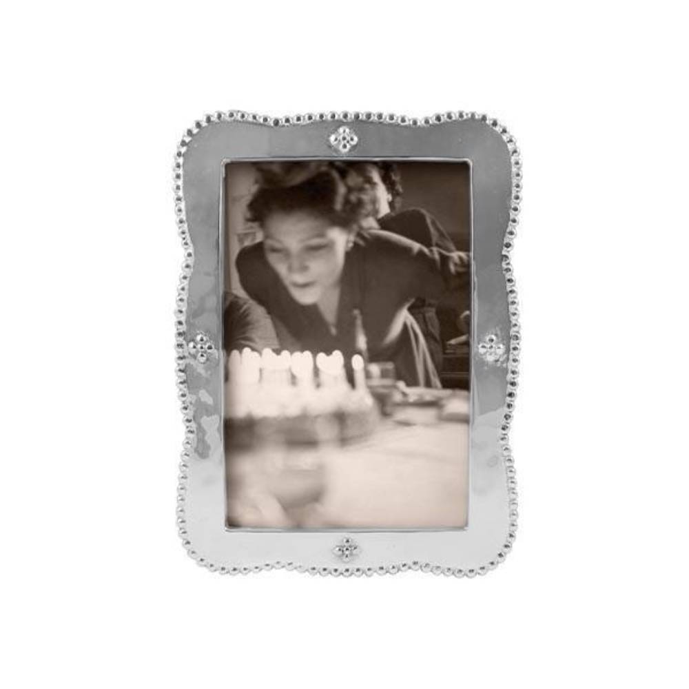 A silver-toned rectangular picture frame with a decorative beaded border and small corner embellishments, holding a black-and-white portrait photo of a person blowing out candles.