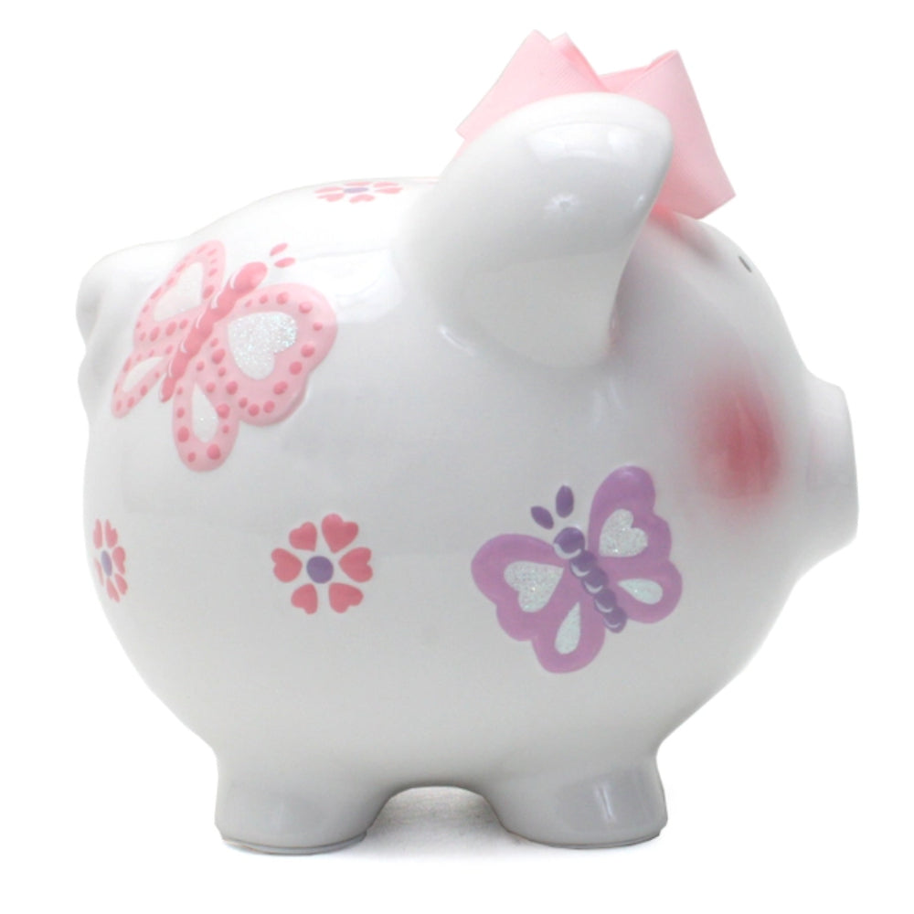A white ceramic piggy bank with pink and purple butterfly decorations, pink ears, and a pink bow on top.
