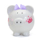 Front photo of a white piggy bank with a pink crown and  purple bow on on a white background