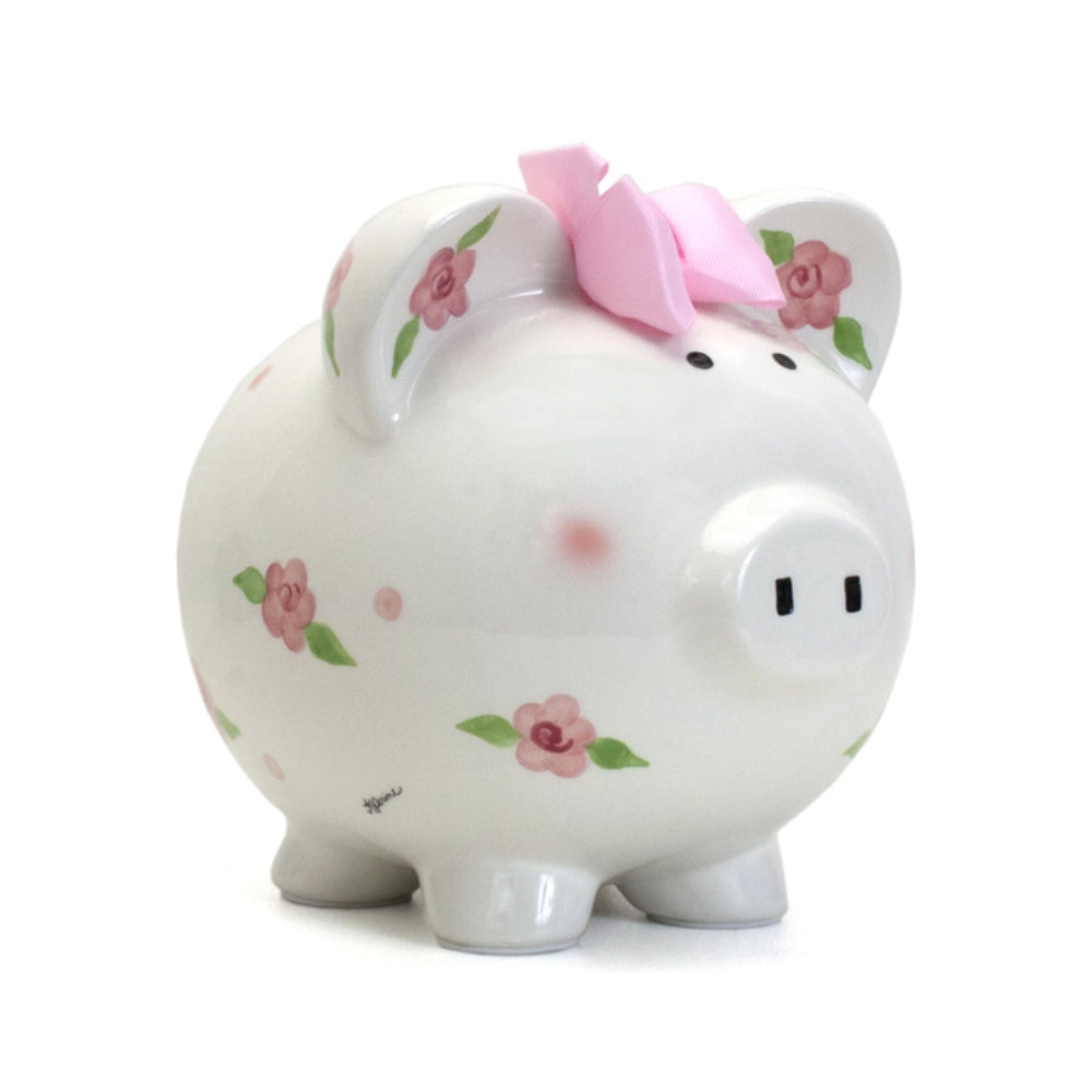A white ceramic piggy bank with floral patterns and pink ribbon detail on the top.