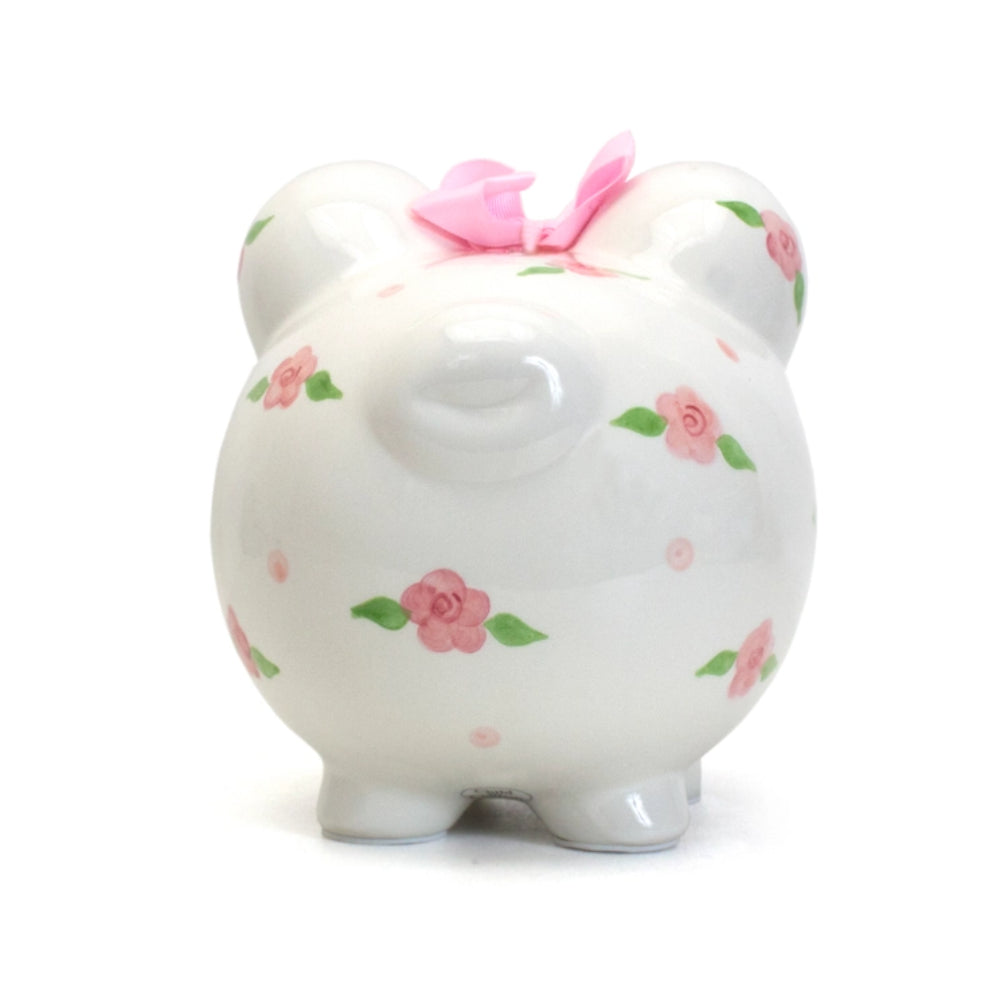 A white ceramic piggy bank with floral patterns and pink ribbon detail on the top.