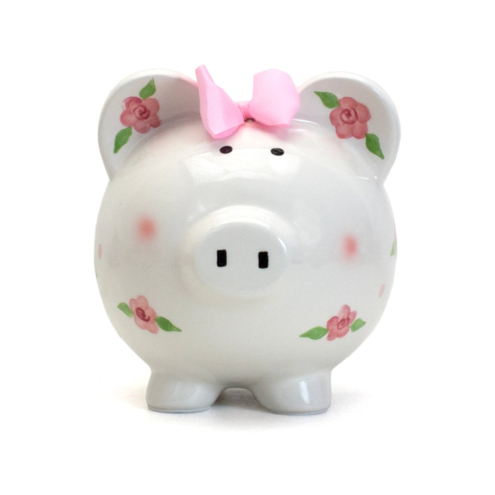 A white ceramic piggy bank with floral patterns and pink ribbon detail on the top.
