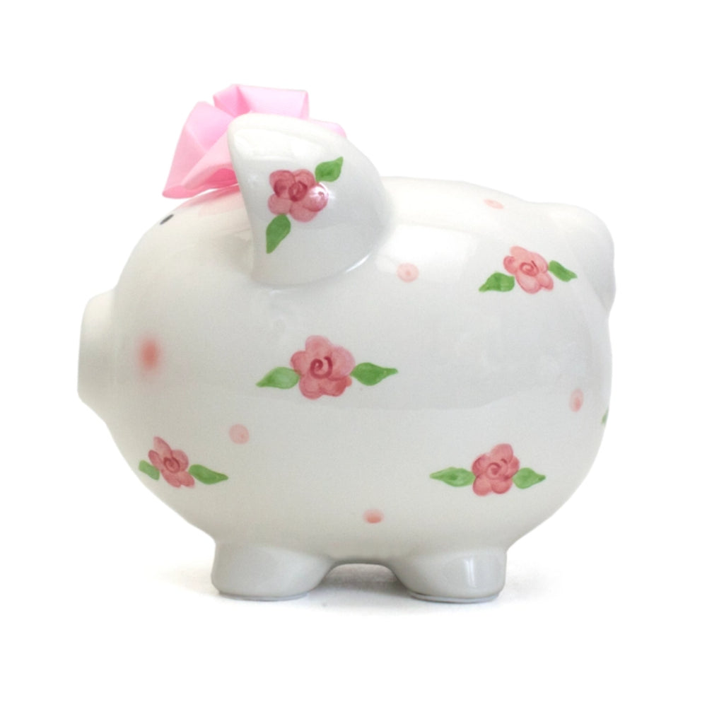 A white ceramic piggy bank with floral patterns and pink ribbon detail on the top.