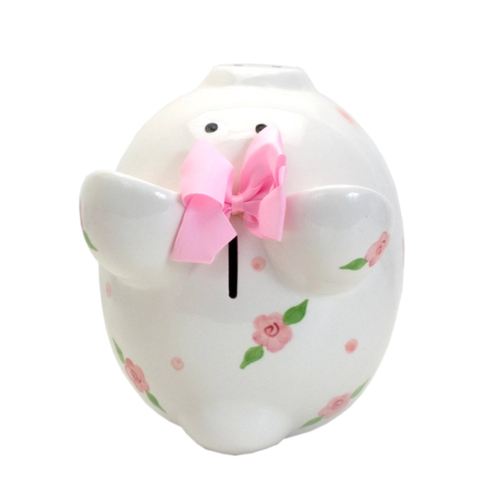 A white ceramic piggy bank with floral patterns and pink ribbon detail on the top.