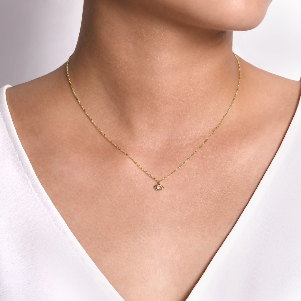 Gold necklace with a pendant on a person wearing a white top