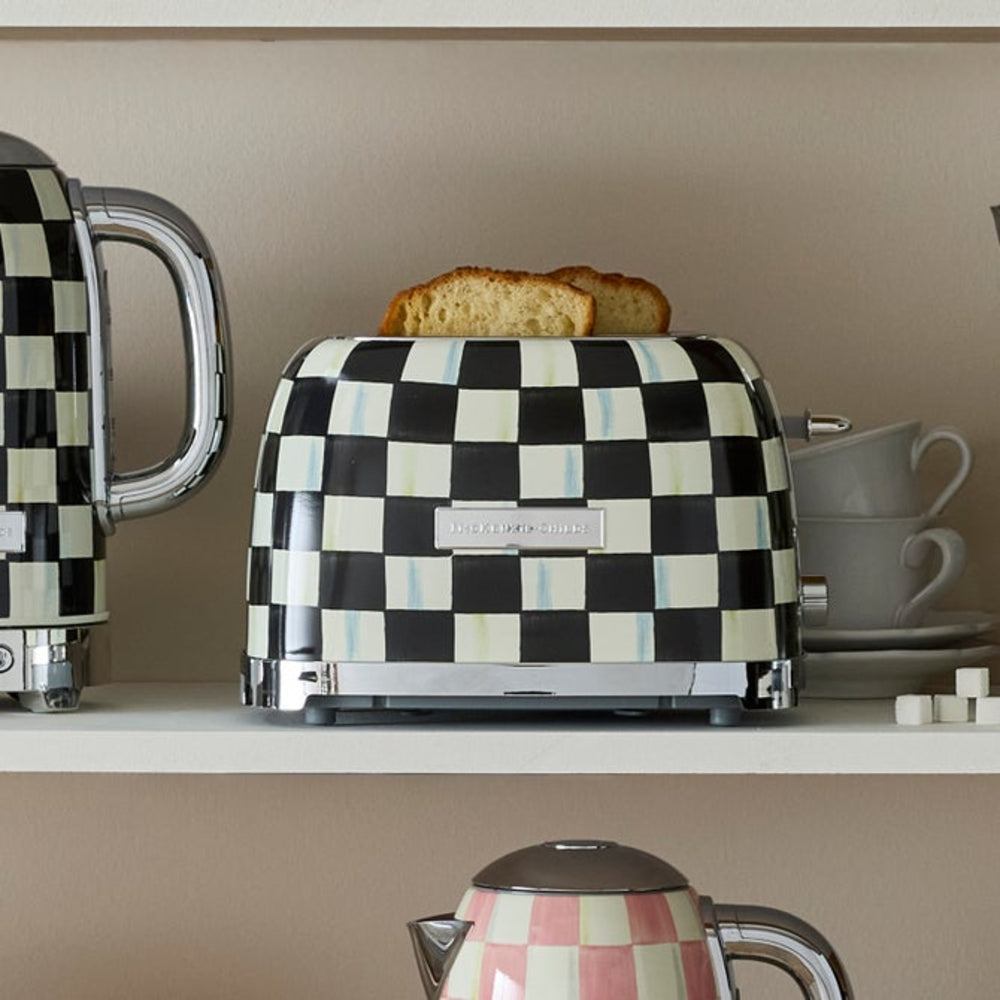 A retro-style checkered toaster with two slices of toast on top, displayed on a kitchen shelf alongside matching checkered teapots and cups.