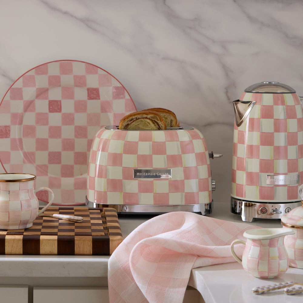 Pink and white checkered toaster and kettle on a marble countertop with a plate and cups.