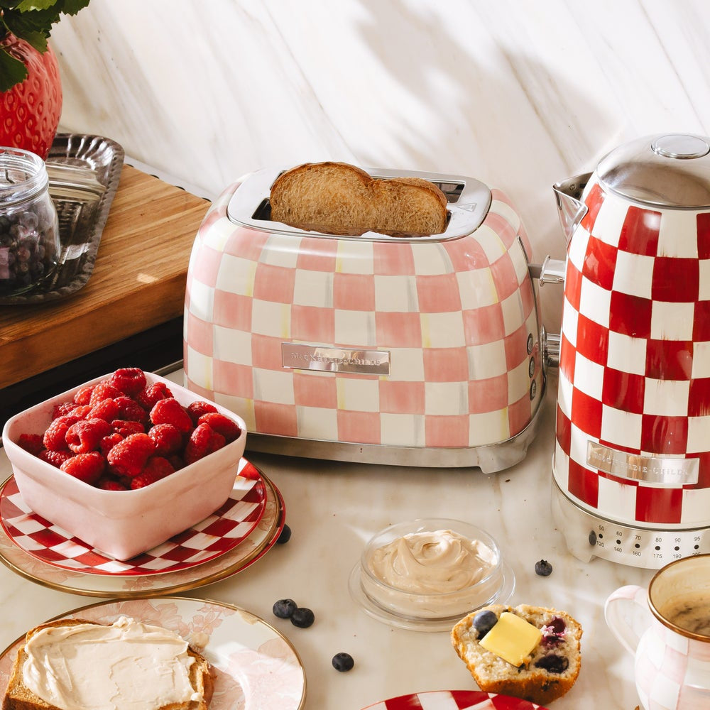 Checkered toaster with toast, bowl of raspberries, and other breakfast items on a table.