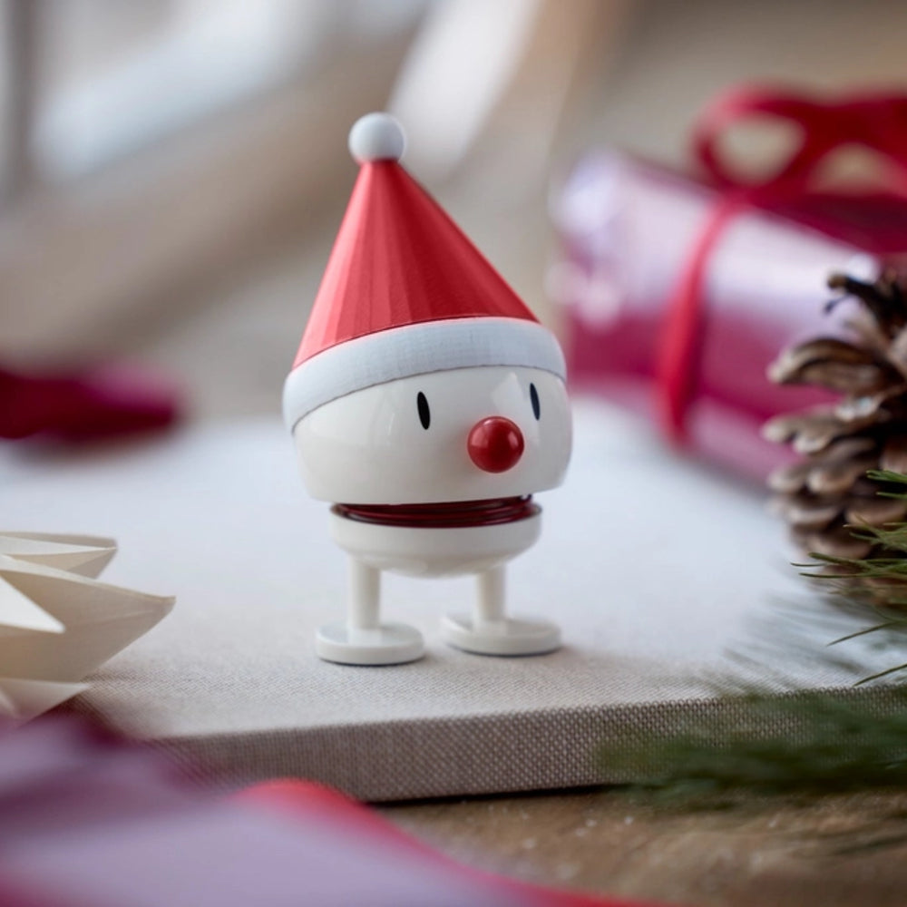 Small figurine wearing a Santa hat on a surface with Christmas decorations.