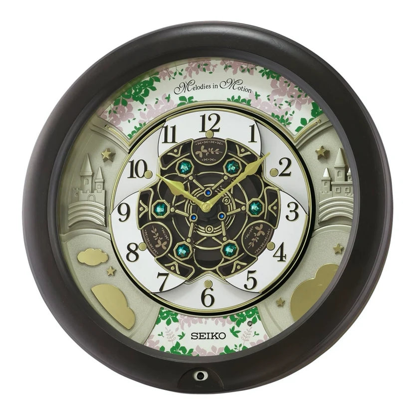 A round Seiko wall clock featuring a fantasy garden design with castle illustrations, pink cherry blossoms, and a central gold-toned mechanical dial on a white background.