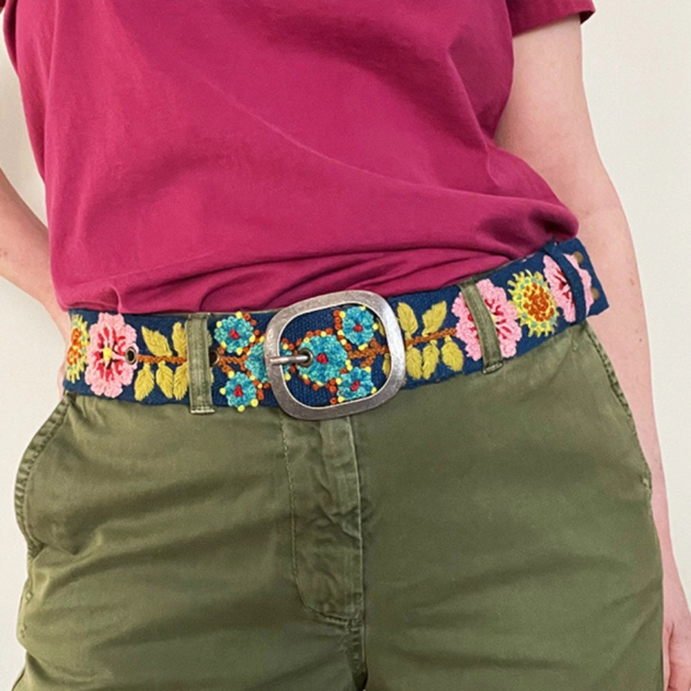 Person wearing a colorful embroidered belt with floral designs on a plain background