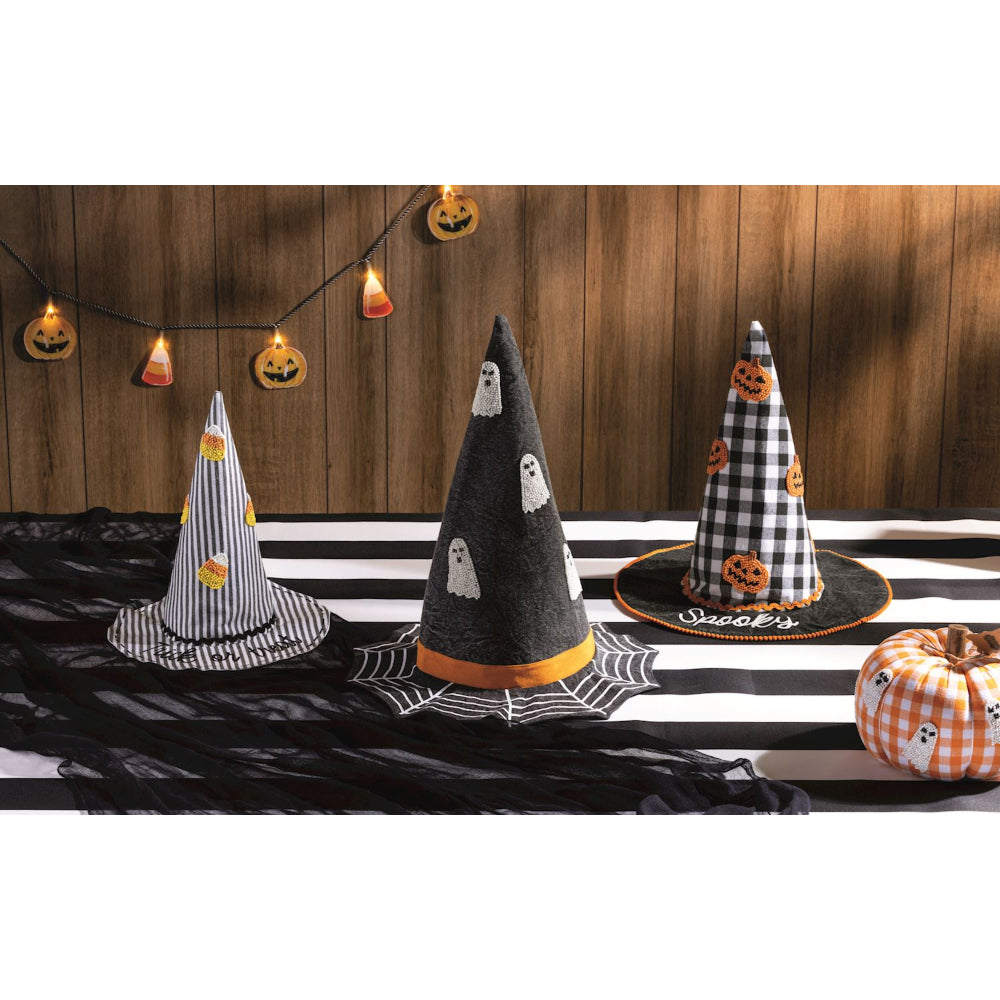 Three Halloween-themed decorative hats on a black and white striped tablecloth with pumpkins and ghost decorations.