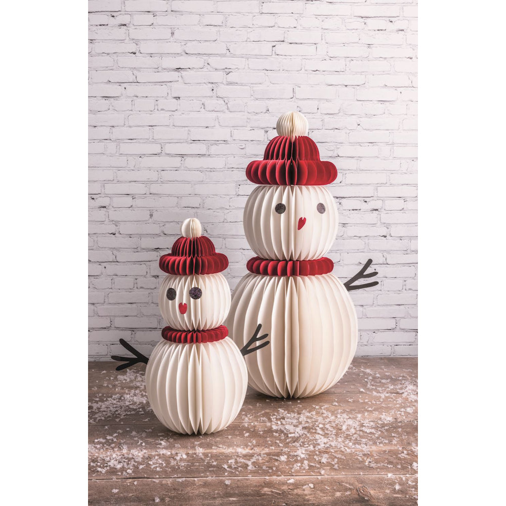 Two snowman-shaped decorative items with red hats and scarves on a wooden surface with a white brick wall background.