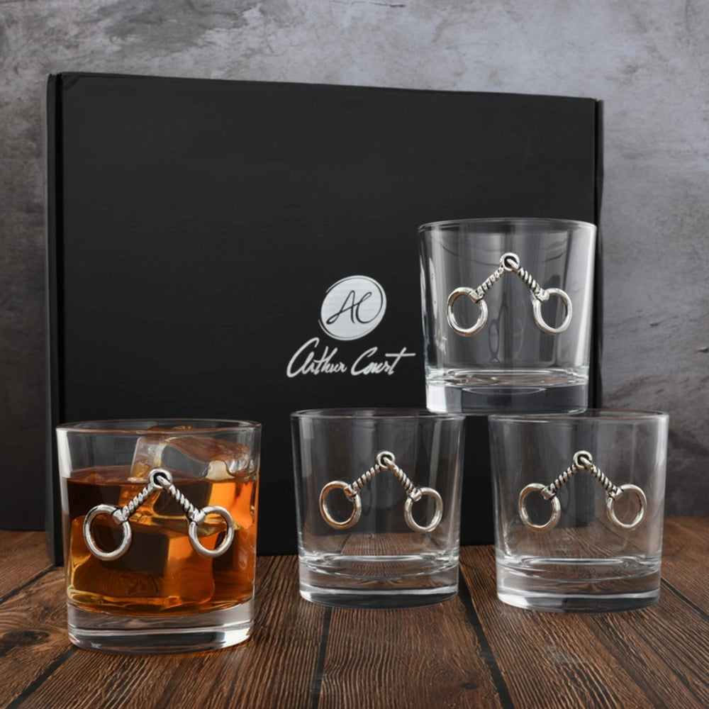 Set of four glass tumblers with metal embellishments on a wooden surface, with a black box in the background.