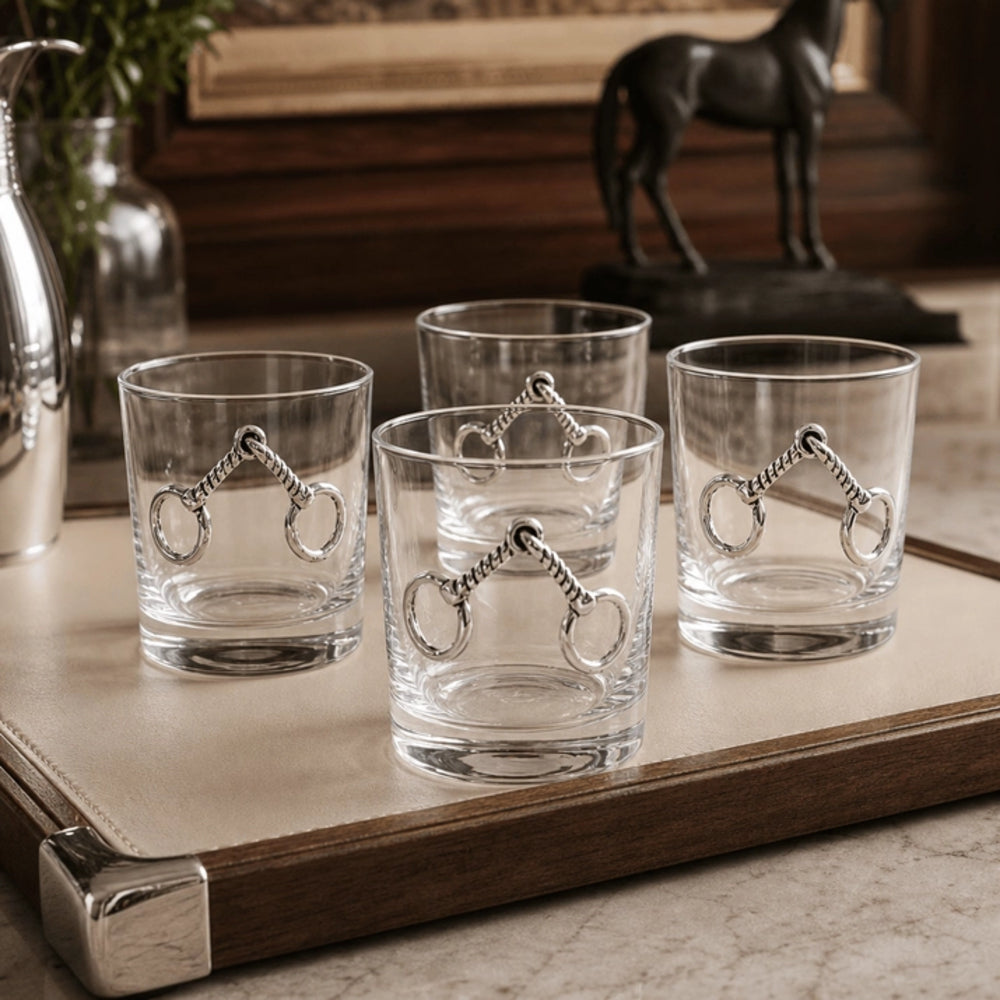 Four clear glass rocks with silver horsebit motifs, arranged on a beige tray with a wooden edge in a styled interior setting.