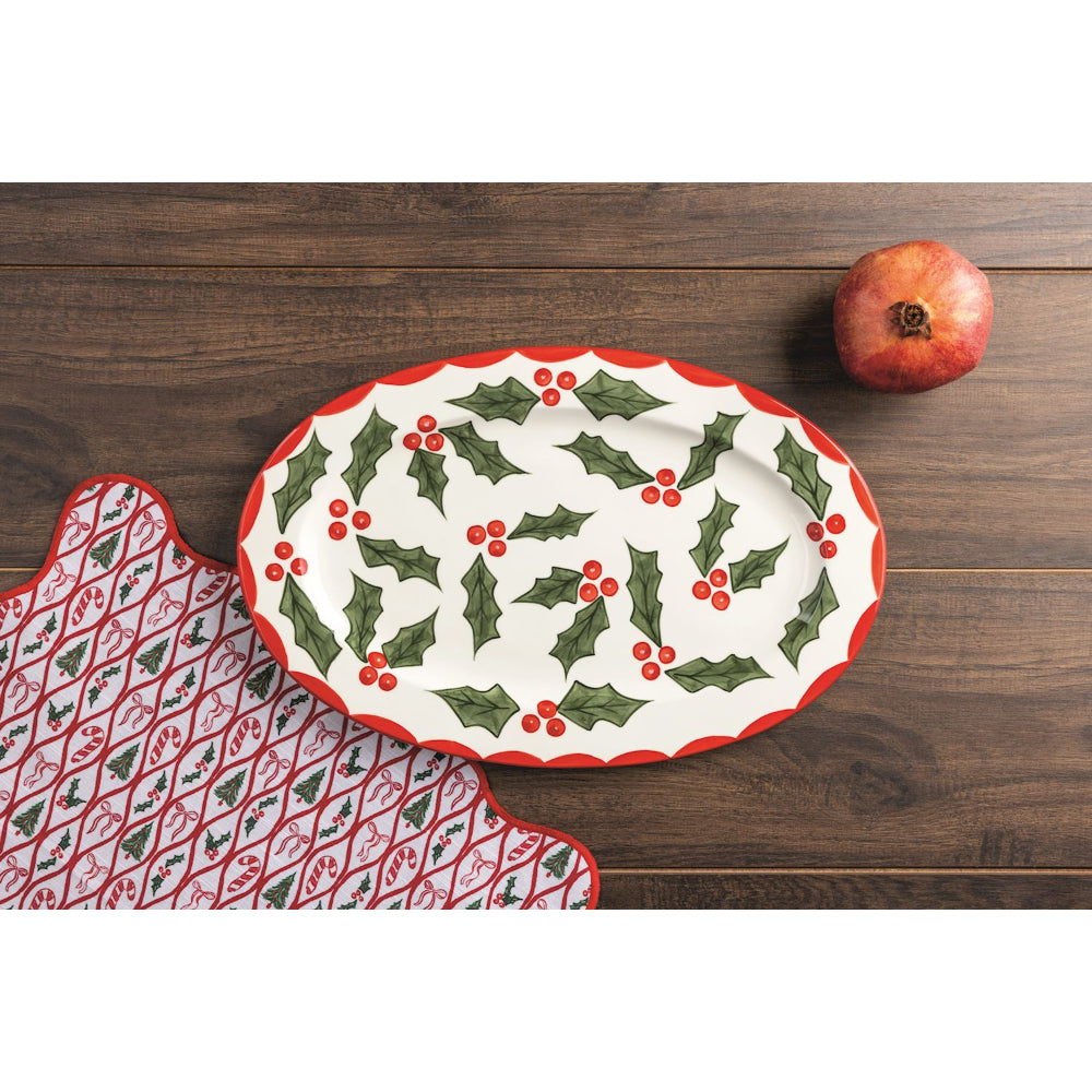 Decorative plate with holly design on a wooden surface with a pomegranate.